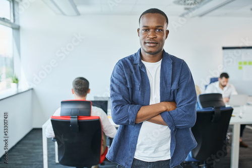 Portrait of creative young man standing in startup office with arms crossed