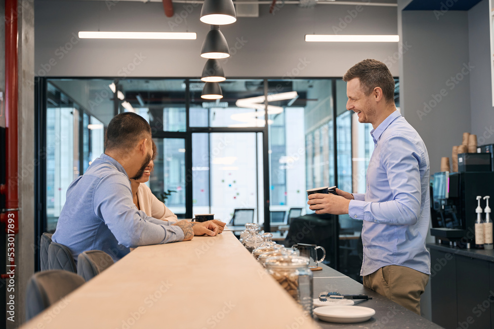 Joyous company employee and his two colleagues in office kitchen Joyous company employee and his two colleagues in office kitchen