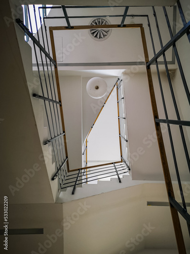 Looking up to Rectangular staircase with light wooden handrail and white ceiling