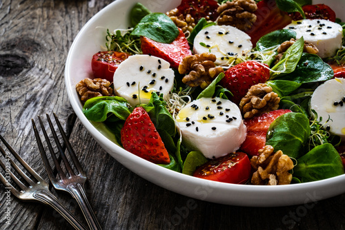 Fresh salad - goat cheese, strawberries, walnuts, cherry tomatoes and leafy greens on wooden table
