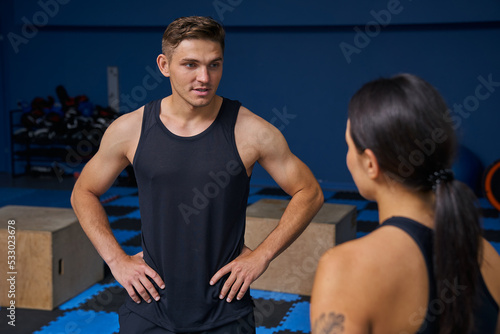 Personal trainer looking at the brunette woman while having conversation with her at the gym