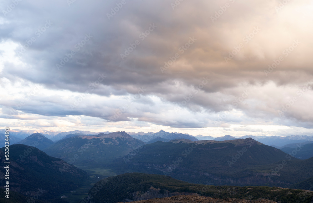View of the mountains and forest at sunset, under a cloudy sky. 
