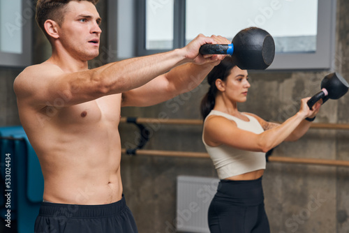 Athletic man and woman lifting and swinging heavy kettlebell, while training