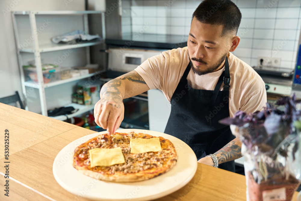 Focused cook putting finishing touches on fresh pizza Focused cook putting finishing touches on fresh pizza