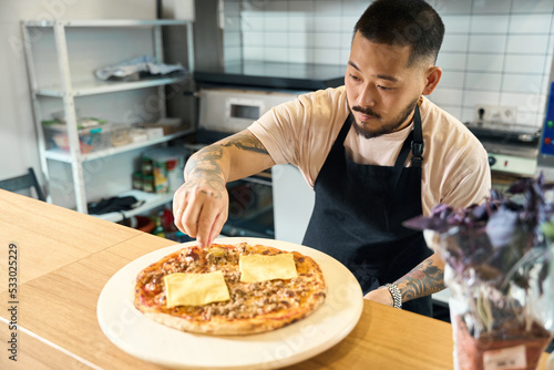 Focused cook putting finishing touches on fresh pizza