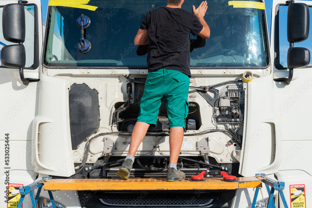 Operator on a scaffold installing a windshield on a truck, fixing it with adhesive tape and with one of the suction cups still attached to the glass. Operator on a scaffold installing a windshield on a truck, fixing it with adhesive tape and with one of the suction cups still attached to the glass.