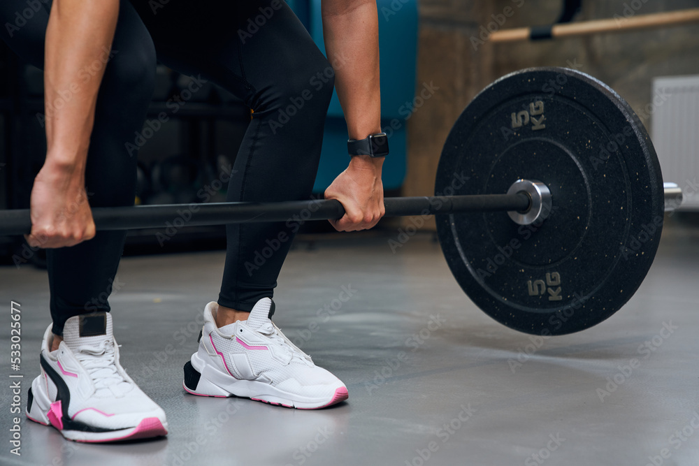 Well-trained female squatting and lifting a barbell with heavy weights at the gym Well-trained female squatting and lifting a barbell with heavy weights at the gym