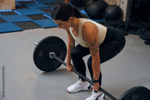 Attractive female bodybuilder performing exercises with barbell in a gym
