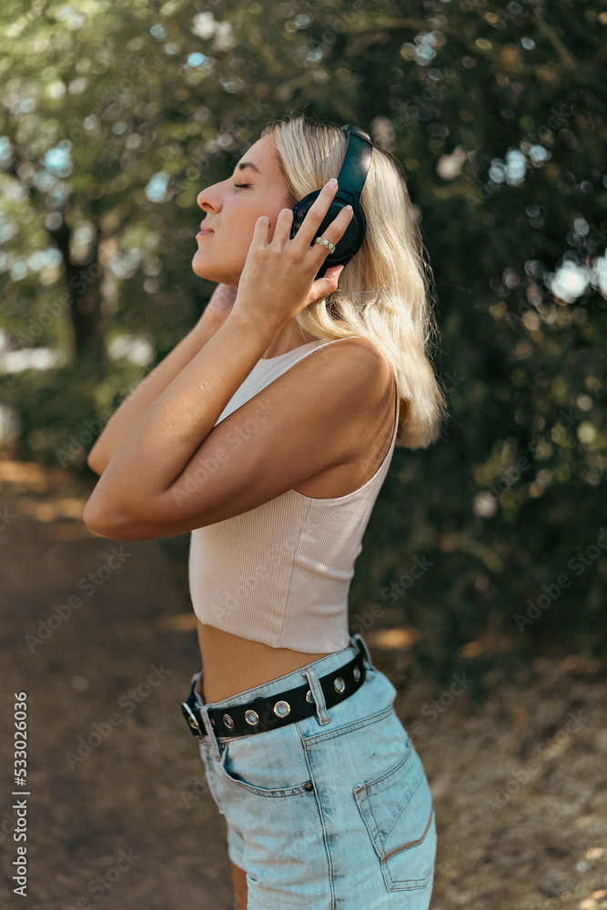 YOUNG WOMAN LISTENING TO MUSIC WITH HEADPHONES IN THE PARK