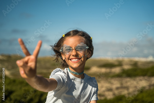 Positive little child shoving victory gesture to her friend while spending time at the green nature