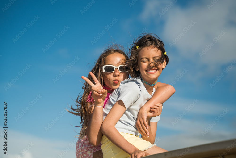 Smiling kid girls gesturing and embracing while having fun on the bridge