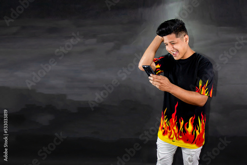 Man with polo shirt with flames holds a smart cell phone. Technology concept on black gradient background