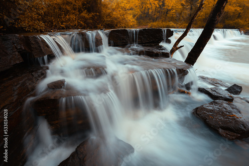 Water cascade flows over a rock stack in an Arkansas creating a scenic waterfall during autumn. 