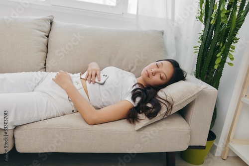 Young Asian woman sleeping on the couch at home with her eyes closed, very tired and resting to feel good