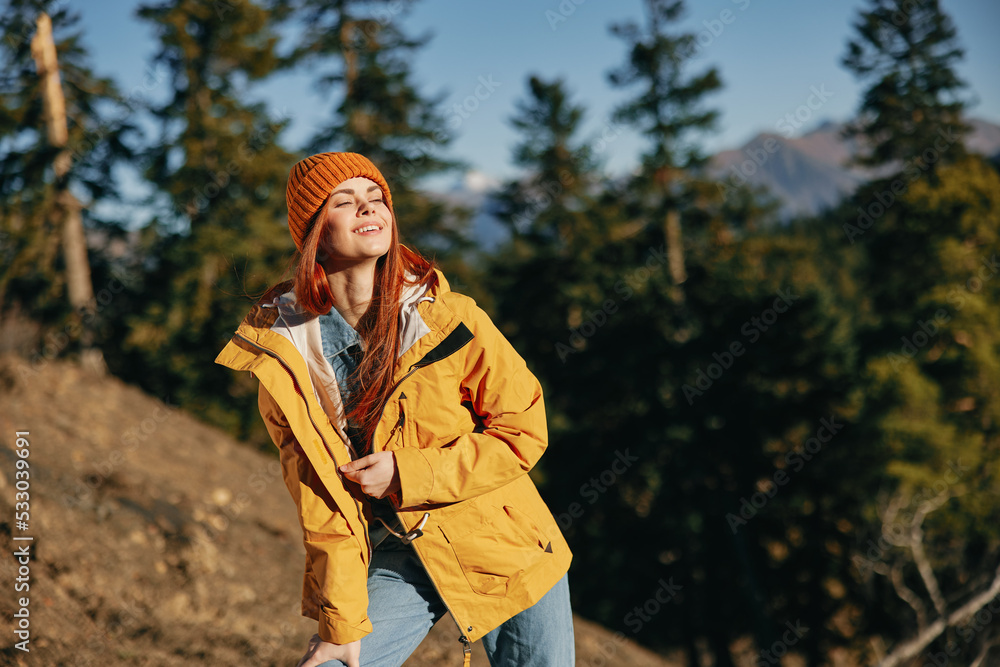 Woman red hair on a hike in the mountains walking a smile and look at the view of nature autumn in a yellow raincoat and hat full-length happiness and freedom Woman red hair on a hike in the mountains walking a smile and look at the view of nature autumn in a yellow raincoat and hat full-length happiness and freedom