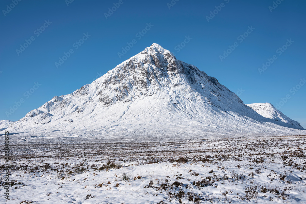 Beautiful iconic landscape Winter image of Stob Dearg Buachaille Etive Mor mountain in Scottish Highlands againstd vibrant blue sky