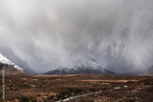 Beautiful Winter landscape image of Stob Dearg Buachaille Etive Mor viewed from Rannoch Moor with snowcapped peak with heavy snow fall passing by the mountain