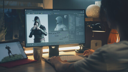 Male 3D designer sitting at the table at home and making animation for video game character, using modern computer and software for creating 3D modeling projects