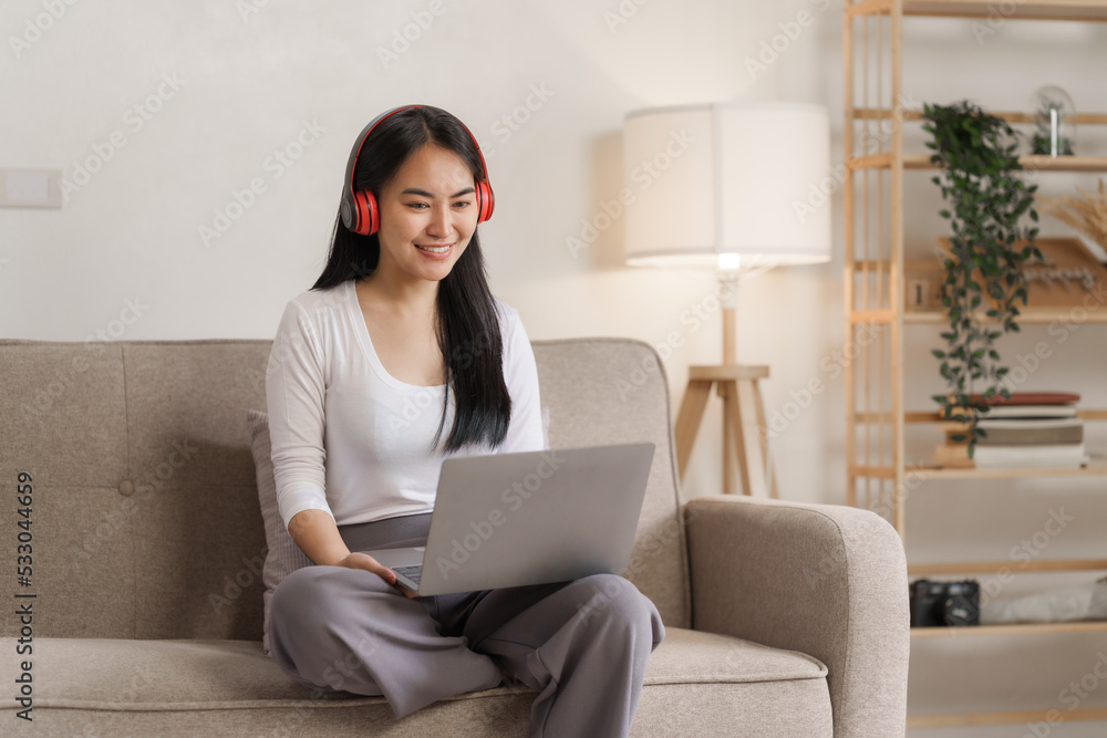 Smiling young asian woman enjoying free time while relaxing with her laptop in living room.. Smiling young asian woman enjoying free time while relaxing with her laptop in living room..