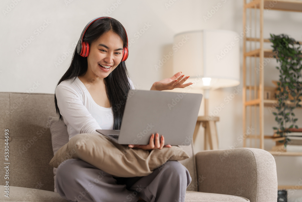 Young happy asian woman using laptop and headphones online meeting with friends via online conference remote meeting. Young happy asian woman using laptop and headphones online meeting with friends via online conference remote meeting.