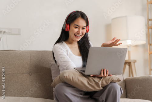 Young happy asian woman using laptop and headphones online meeting with friends via online conference remote meeting. © NanSan
