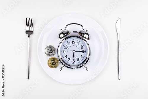 Top view alarm clock on a white plate with a knife and fork on a white background. Intermittent fasting, ketogenic diet, weight loss, meal plan and healthy eating concept