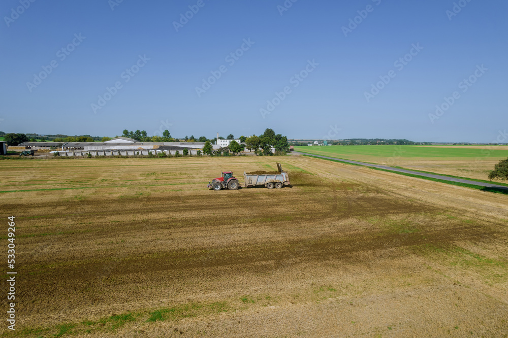 The tractor scatters manure on the field from the trailer. Feeding the soil. Natural fertilizer. View from above.