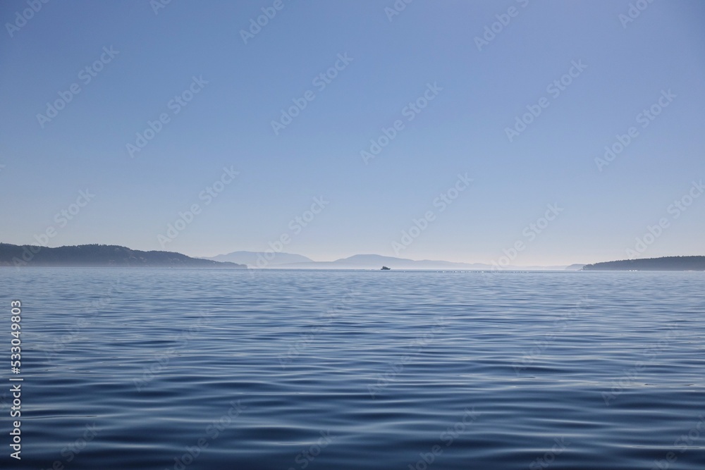 A beautiful seascape view of a boat in the far distance sailing across the open sea in the gulf islands, british columbia, canada
