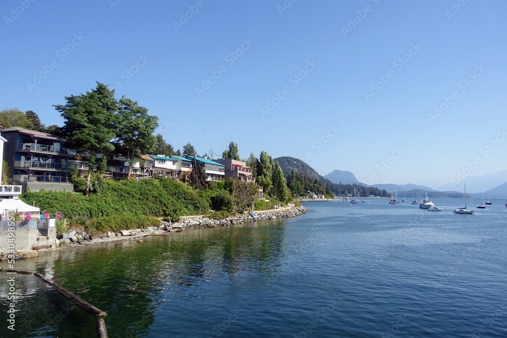 A beautiful view of the town of Gibsons along the sunshine coast, with boats anchored in the bay, and the coast mountains in the background, on a beautiful summer day.