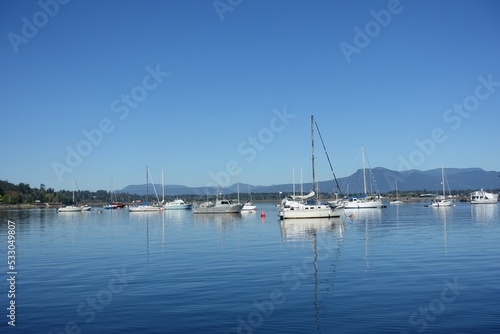 A beautiful sunny summer day in the gulf islands with sailboats resting on the calm ocean surrounded by scenic forested coastline