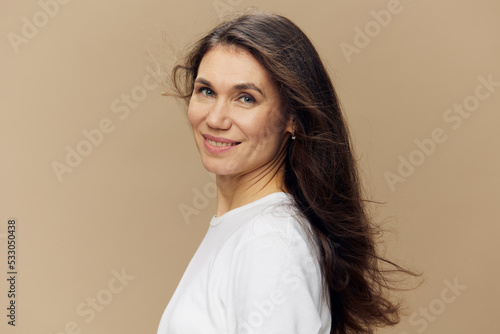 portrait of a sweet, beautiful, charming, pleasant woman with black hair, blowing in the wind, in a white T-shirt. Studio photo on a plain background