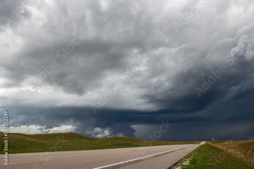 A storm begins to form a wall cloud underneath its base along a highway in a vast grassland.