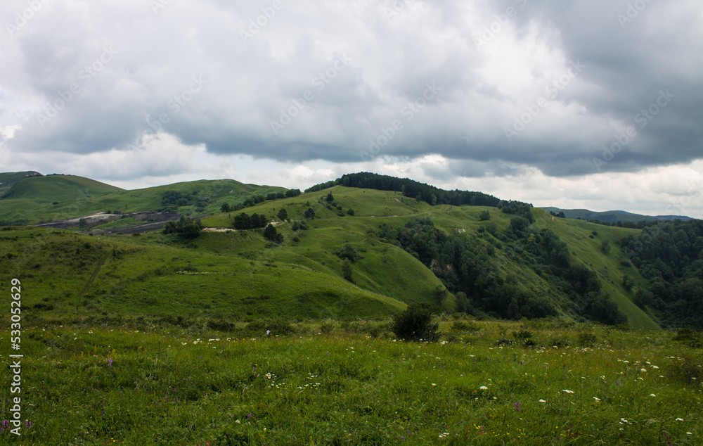 Fototapeta premium Panoramic top view of a beautiful valley with trees and hills and a blurred horizon against a cloudy dramatic sky in Kislovodsk russia