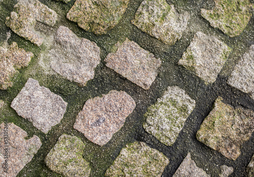 Stone pavement texture. Granite cobbled pavement background. Traditional rustic pavers. Cobblestones with verdigris