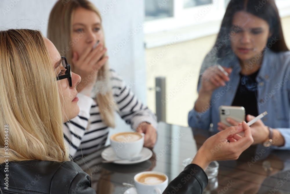 Women smoking cigarette at table in outdoor cafe Women smoking cigarette at table in outdoor cafe