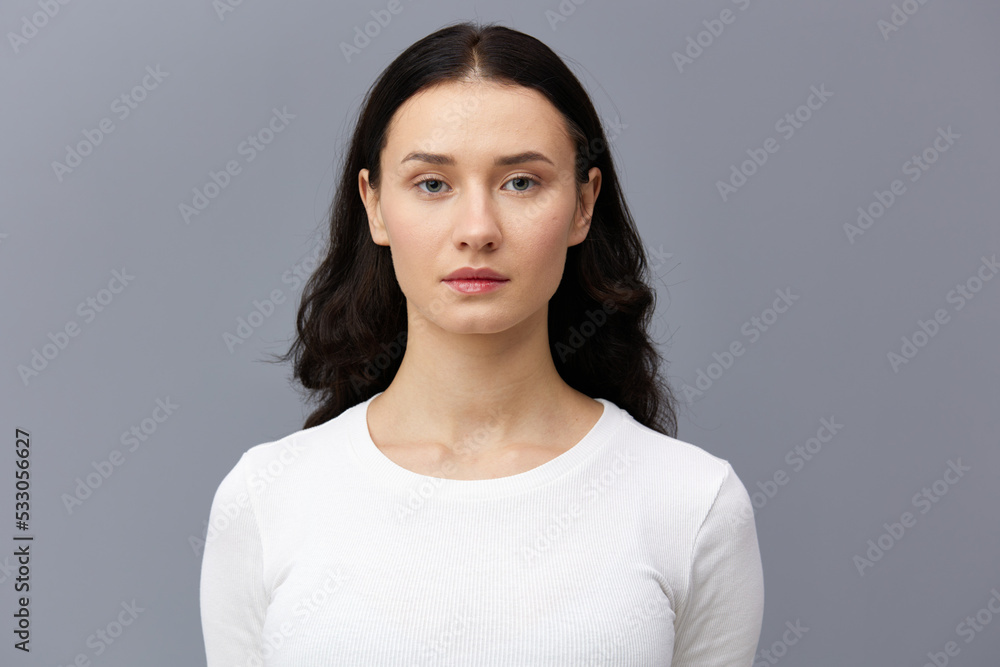a gentle woman stands on a dark background in a tight white T-shirt, calmly lowered her hands down and looks forward a gentle woman stands on a dark background in a tight white T-shirt, calmly lowered her hands down and looks forward