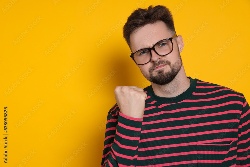 Aggressive man in striped sweatshirt and eyeglasses on yellow background, space for text Aggressive man in striped sweatshirt and eyeglasses on yellow background, space for text