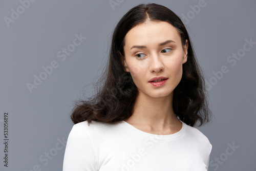 a gentle woman stands on a dark background in a tight white T-shirt  calmly looking forward smiling sweetly