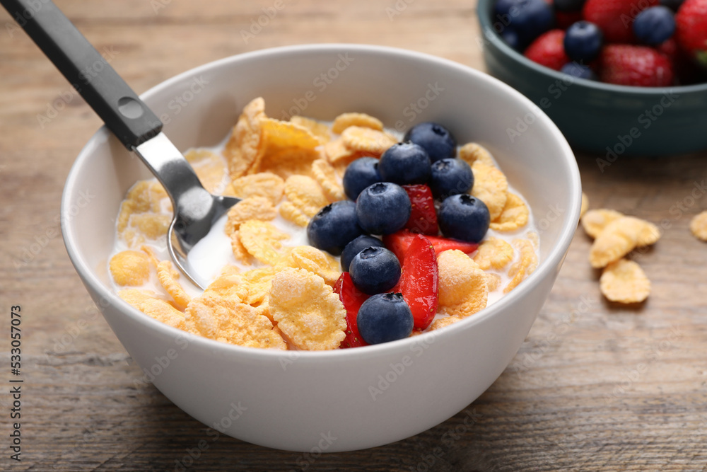 Bowl of tasty crispy corn flakes with milk and berries on wooden table, closeup Bowl of tasty crispy corn flakes with milk and berries on wooden table, closeup