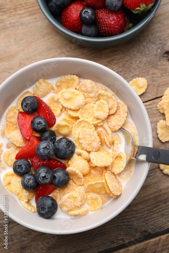 Bowl of tasty crispy corn flakes with milk and berries on wooden table, flat lay