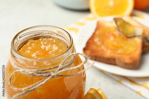 Delicious orange marmalade in glass jar on light table, closeup. Space for text