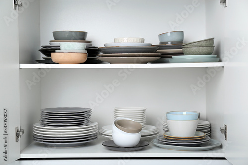Different clean plates and bowls on shelves in cabinet
