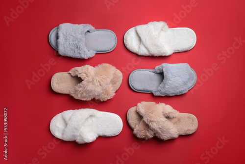 Different soft fluffy slippers on red background, flat lay