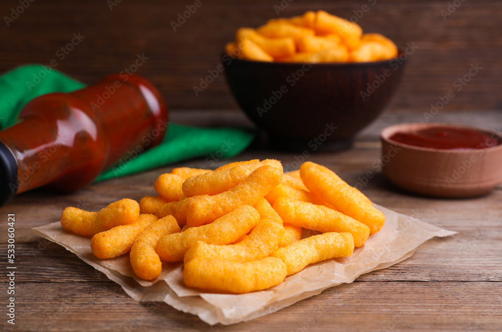 Crunchy cheesy corn snack and ketchup on wooden table, closeup