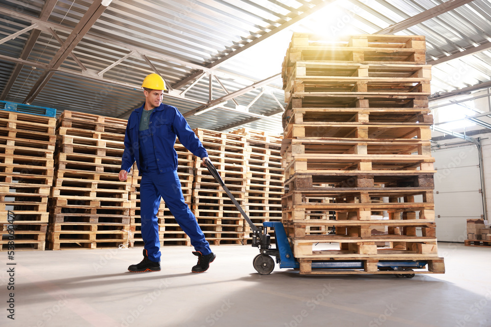 Fototapeta premium Worker moving wooden pallets with manual forklift in warehouse
