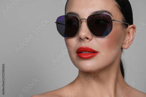 Attractive woman in fashionable sunglasses against grey background, closeup. Space for text