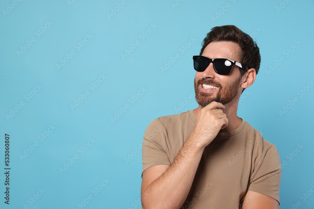 Portrait of smiling bearded man with stylish sunglasses on light blue background. Space for text Portrait of smiling bearded man with stylish sunglasses on light blue background. Space for text