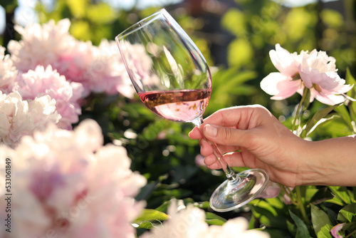 Fototapeta Naklejka Na Ścianę i Meble -  Woman with glass of rose wine in peony garden, closeup