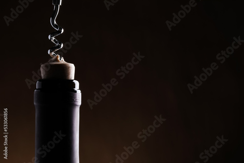 Opening wine bottle with corkscrew on dark background, closeup. Space for text
