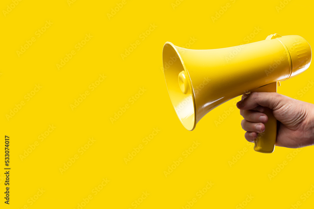 A man's hand holds a yellow megaphone on a bright yellow background. Rumors, fakes, agitation, propaganda, election debates, journalism, media, business, advertising.
